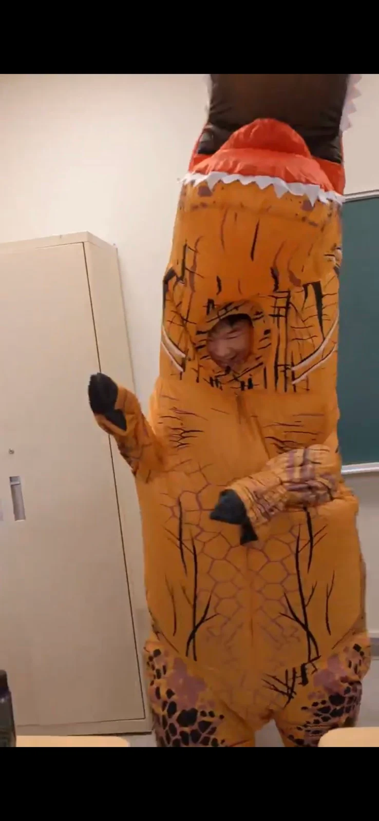 A person peeking out of an inflatable dinosaur costume