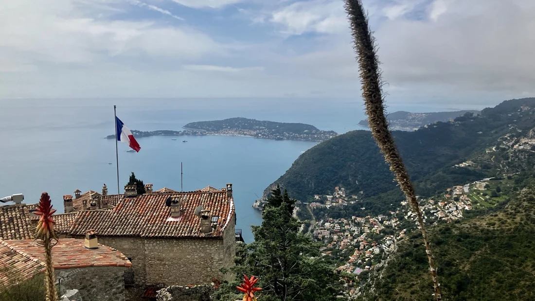 A French flag above tiled rooftops overlooking the Mediterranean coastline