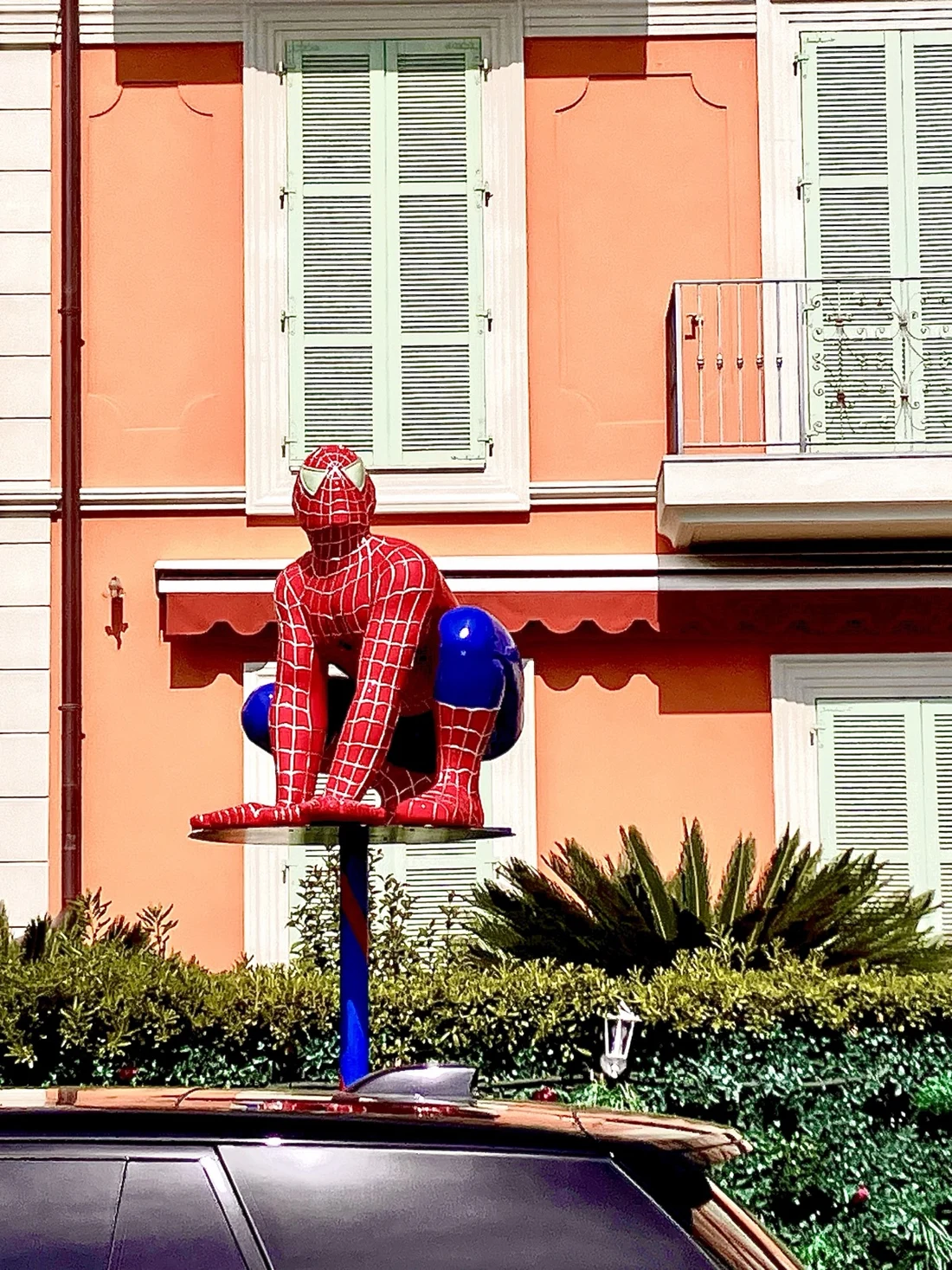 A Spider-Man sculpture above a car beside a coral-colored building