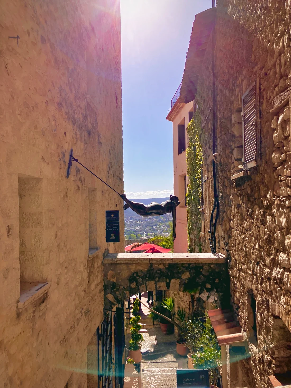 A figure suspended between sunlit stone buildings above a courtyard