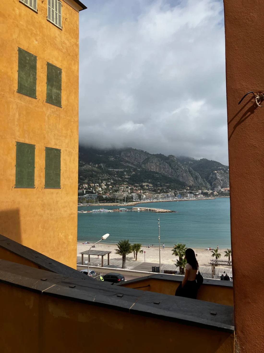 A window framing a turquoise waterfront between yellow walls